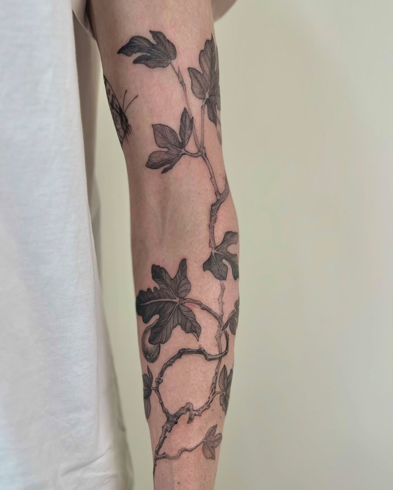 The same fig-vine tattoo as the arm turns, leaves wrapping around